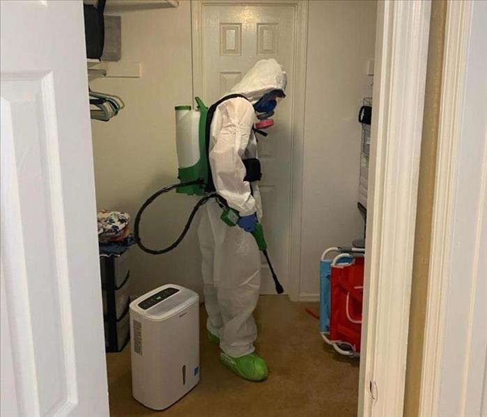 SERVPRO technician in living room with PPE and cleaning equipment