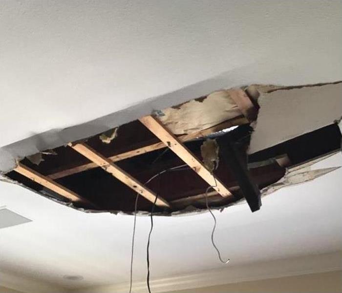 A huge hole in the ceiling of this home with drywall falling to the floor below. 
